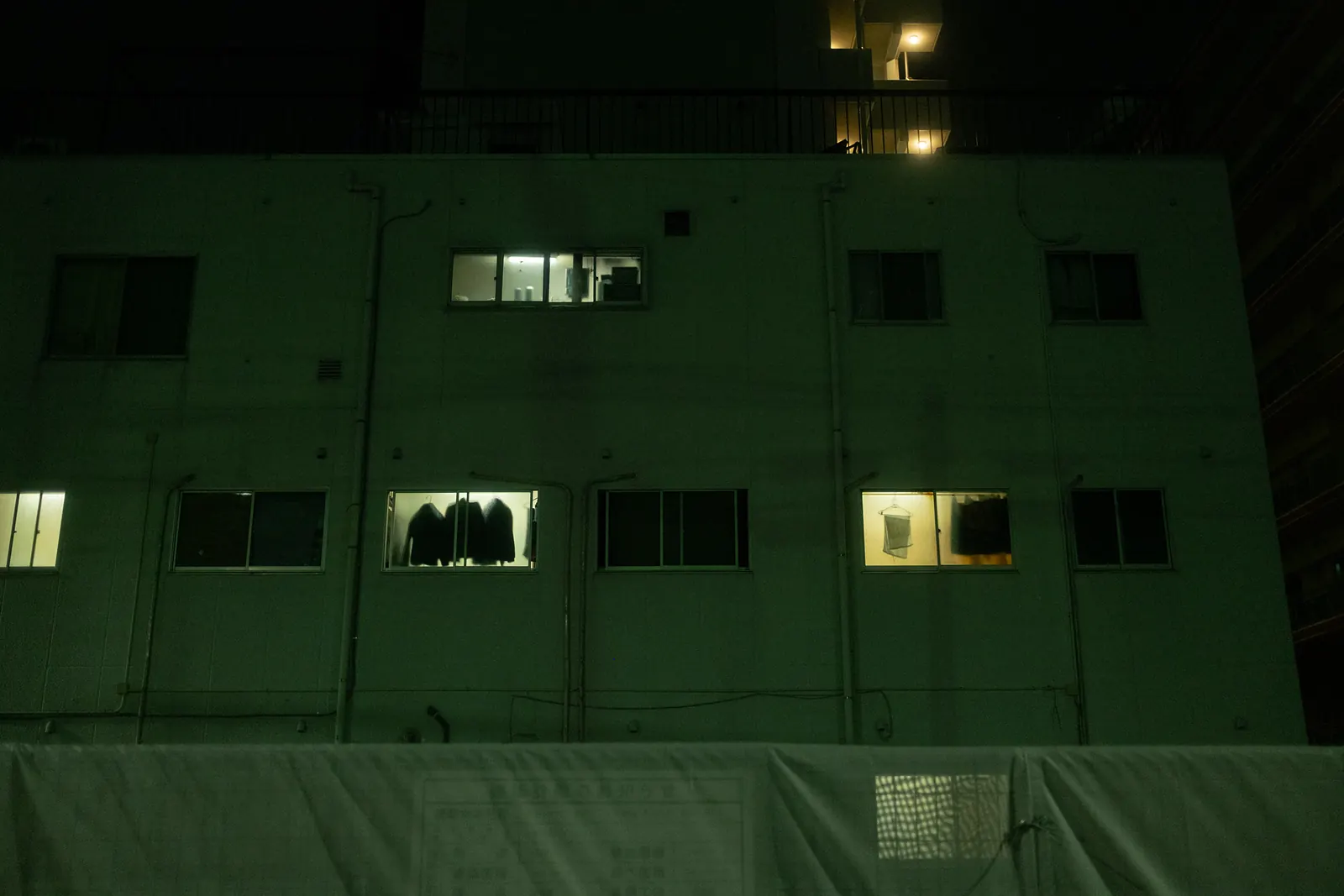 The windows of an apartment block at night, a few lit from inside with clothes hanging.