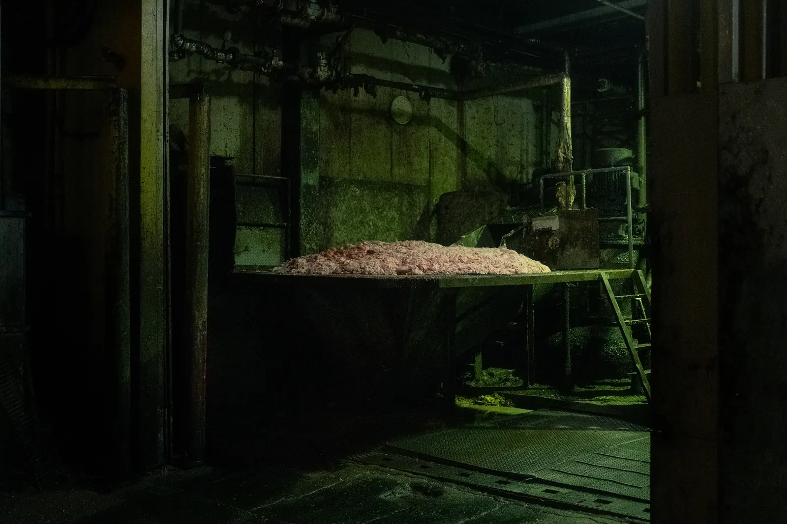 A dim industrial room lit in green, with a platform holding a heap of material.