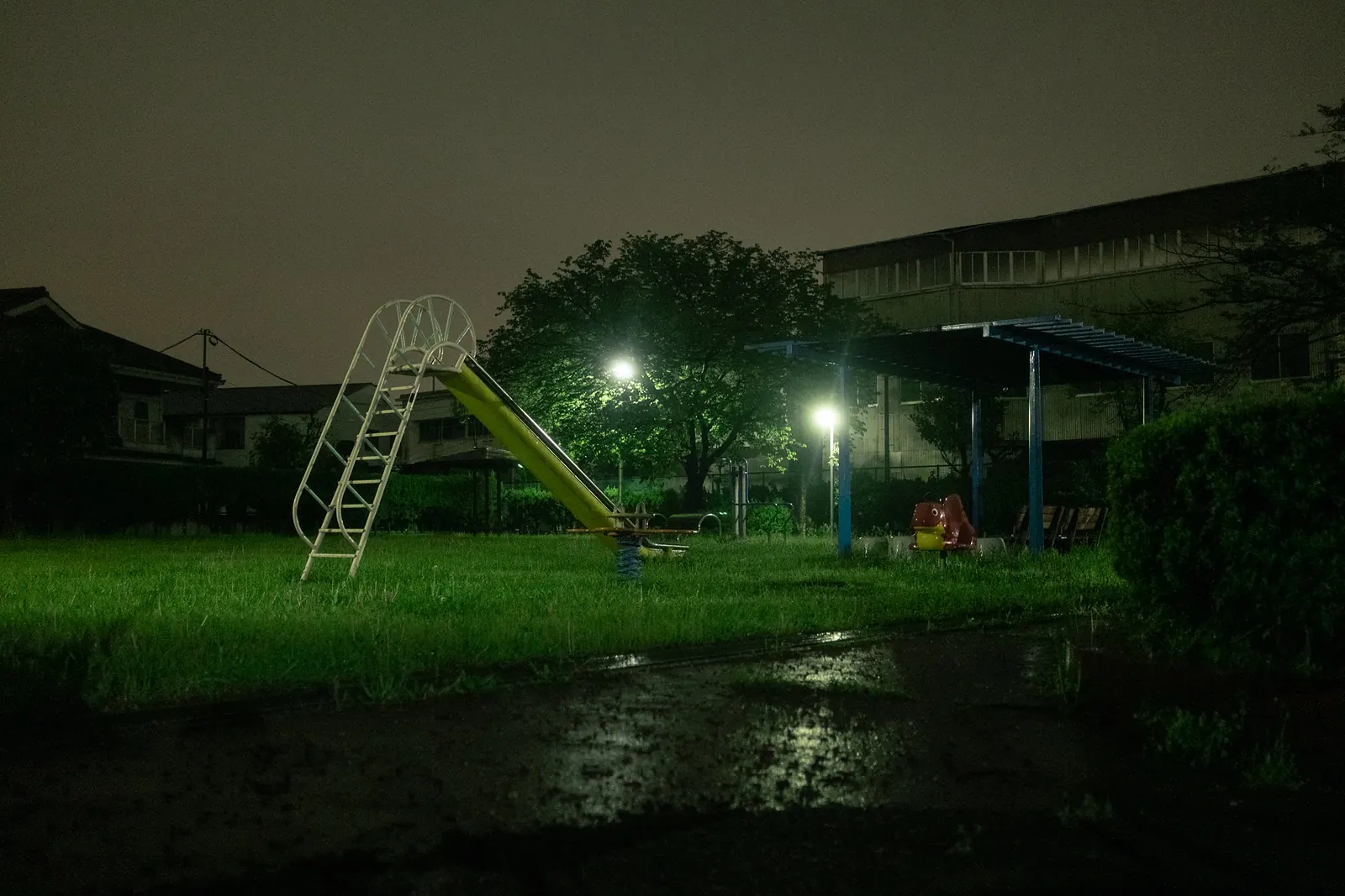 A deserted playground with a slide in green grass under a dark night sky.