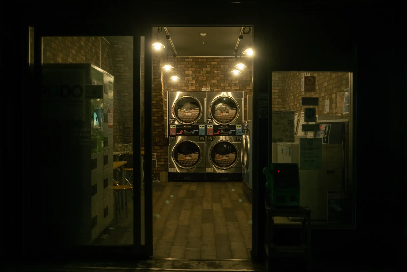 A brightly lit laundromat seen from the dark street, washing machines glowing at the back.