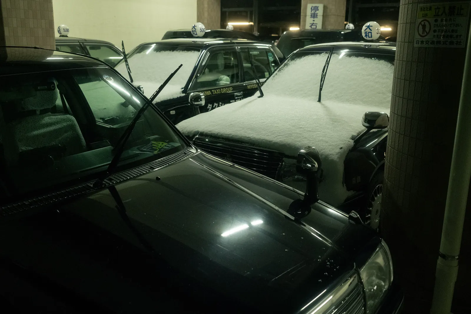 Snow-covered taxis parked close together in a garage.