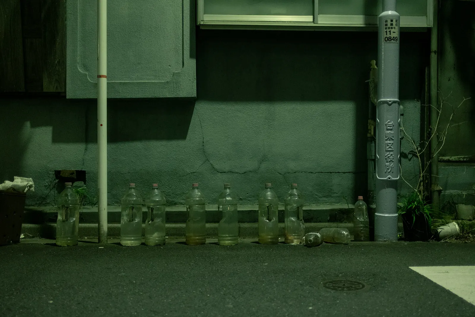A row of plastic bottles lined up against a wall beside a utility pole on a quiet street at night.