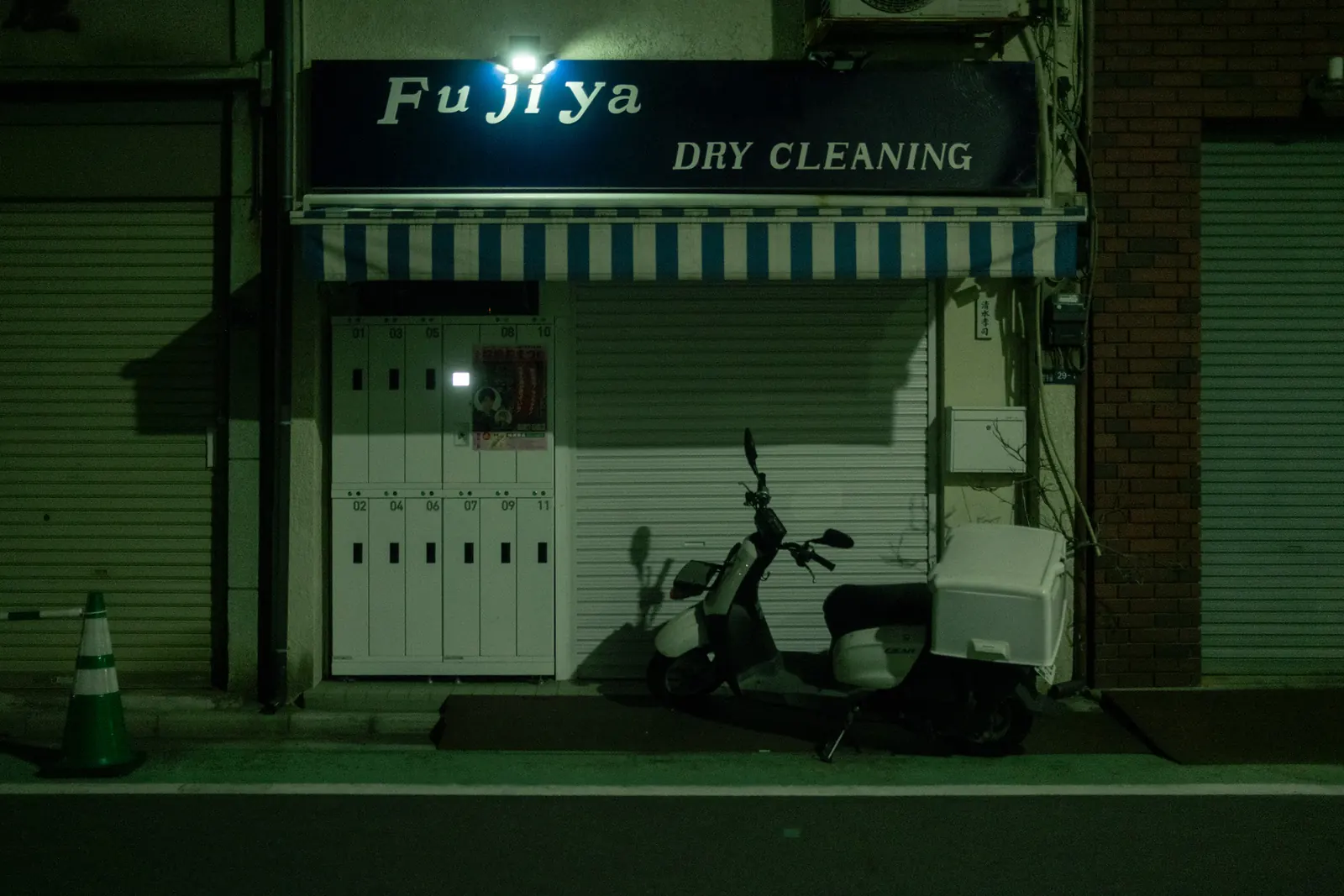 A closed dry cleaner at night with a scooter parked in front of the shutters.