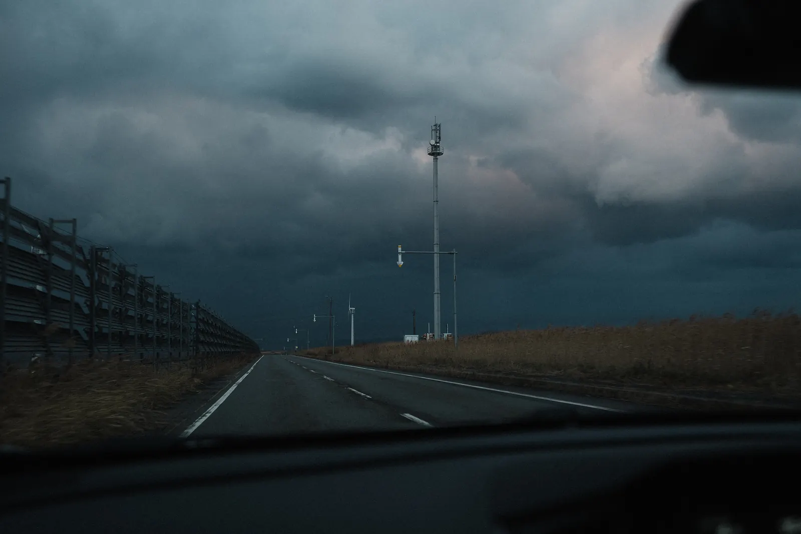 A road beside a barrier under storm clouds, seen through the windshield.
