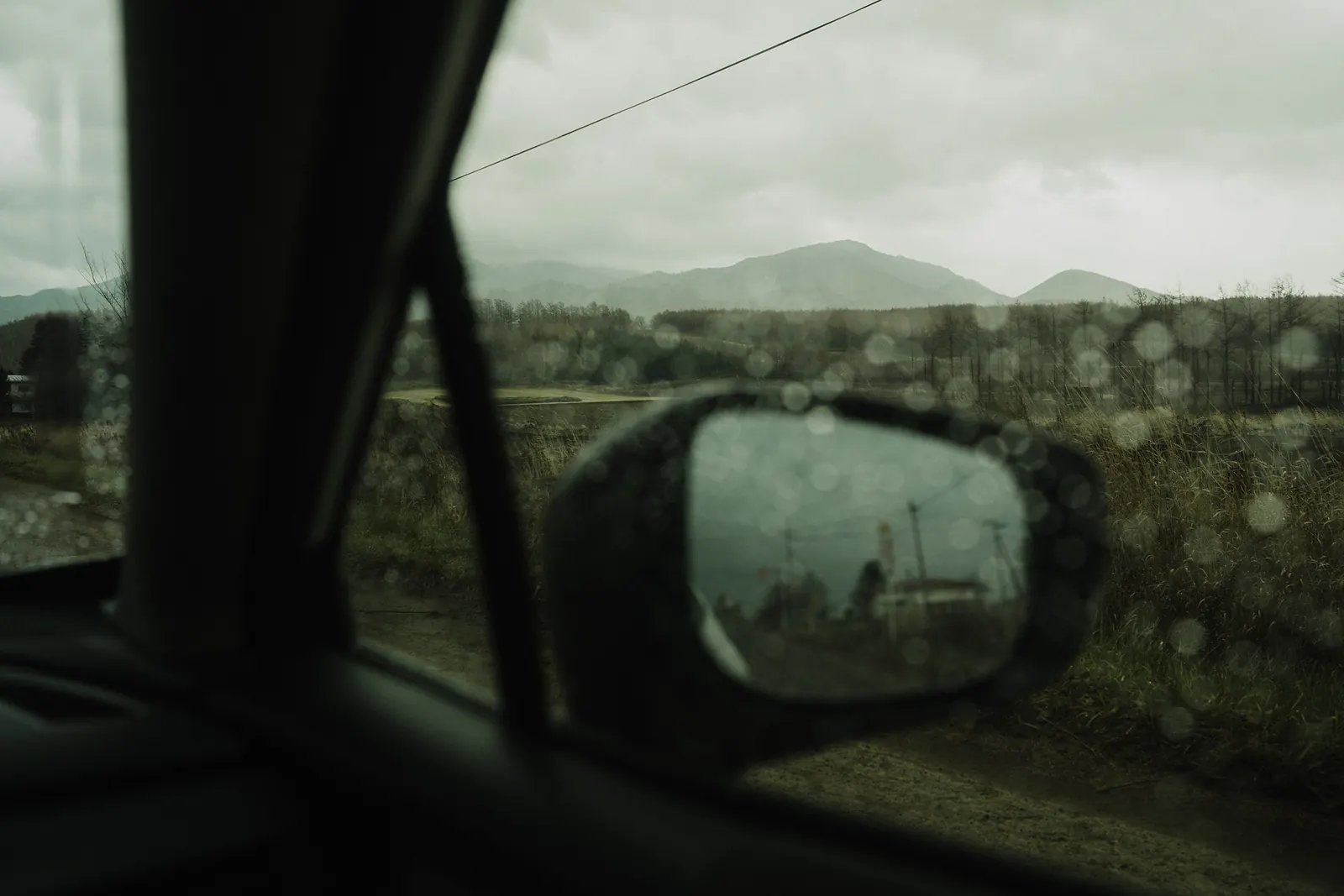 A rain-spotted side mirror in front of misty mountains.