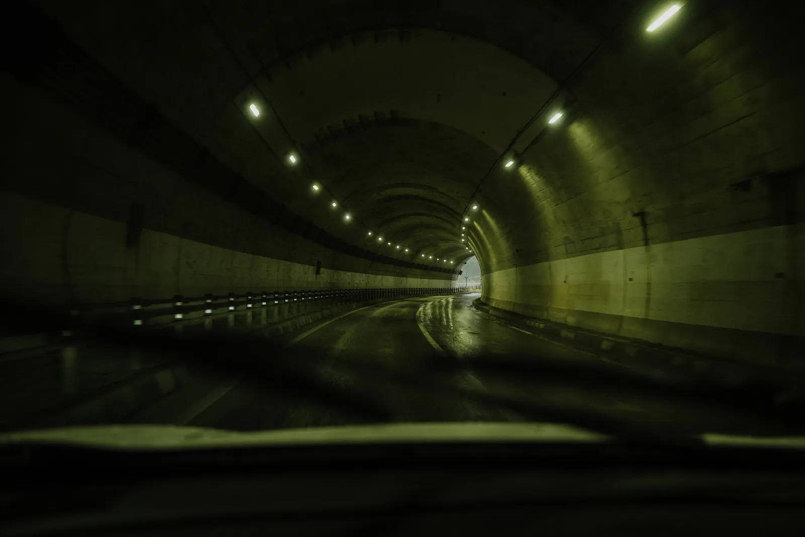 The inside of a tunnel with rows of lights and a wet road.