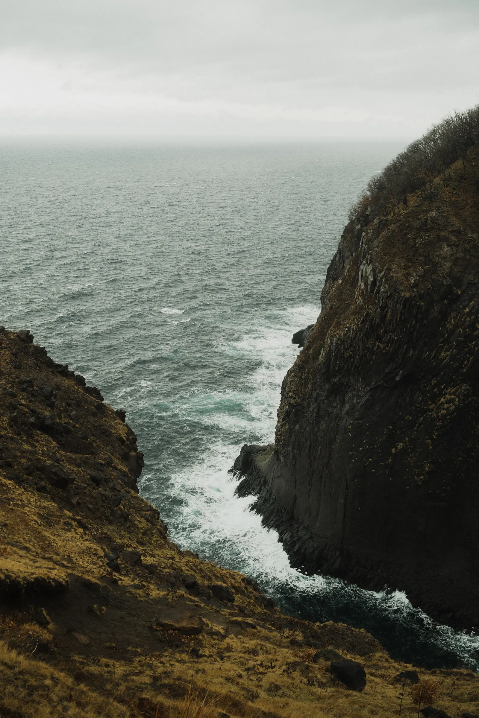 Waves crashing against a dark cliff, seen from above.