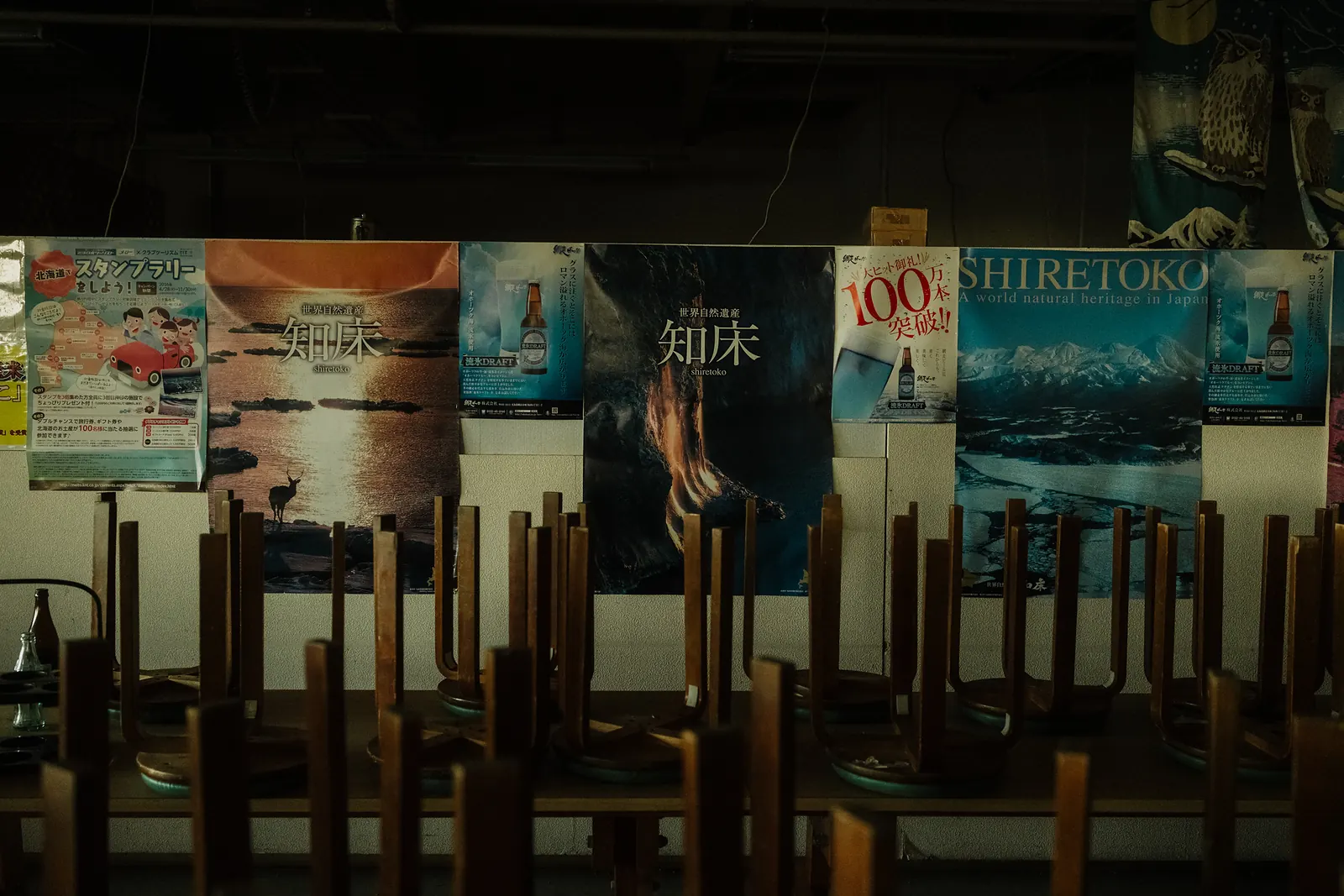 Upturned stools in front of a wall of Shiretoko posters in an empty restaurant.
