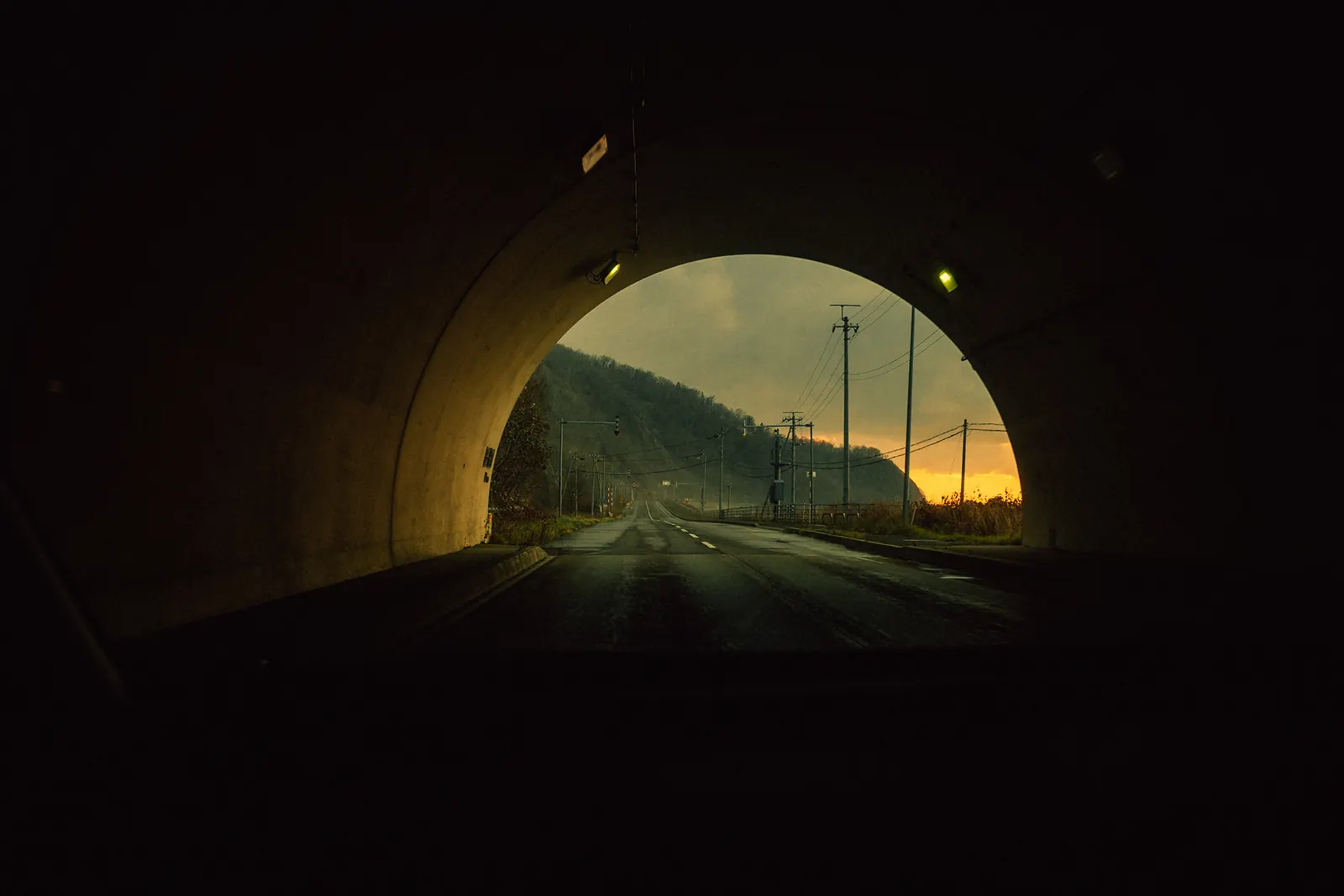 A tunnel opening onto a coastal road at sunset.