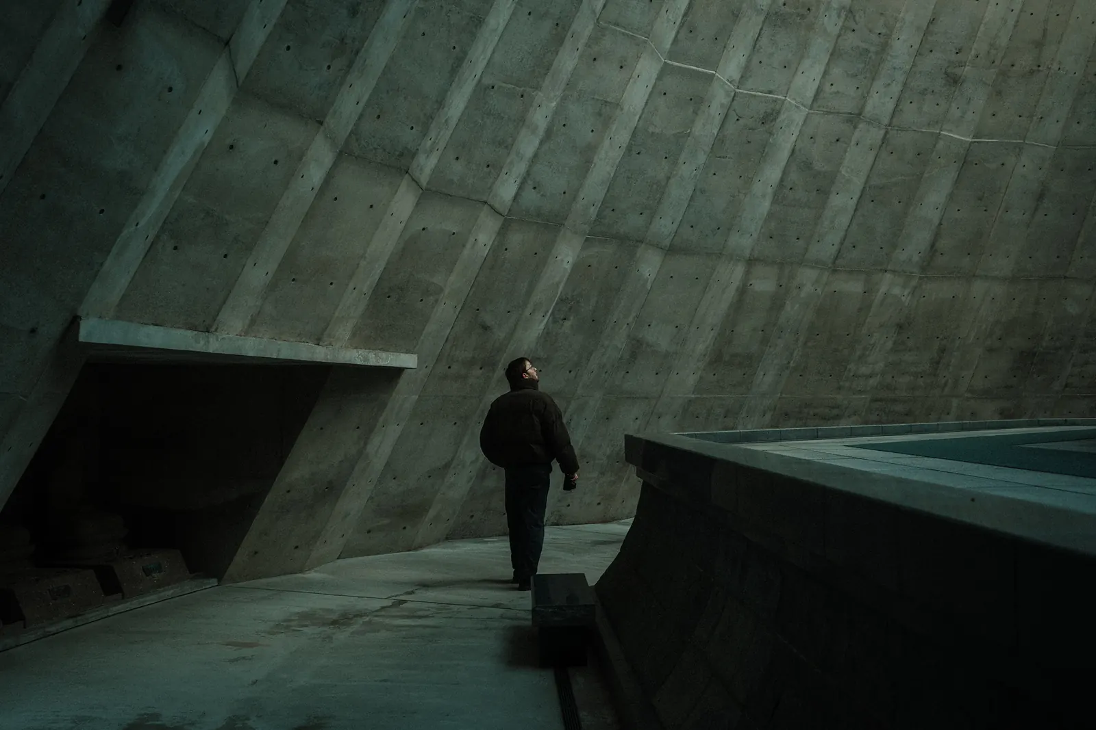 A person walks along a concrete wall in a stark, angular space.