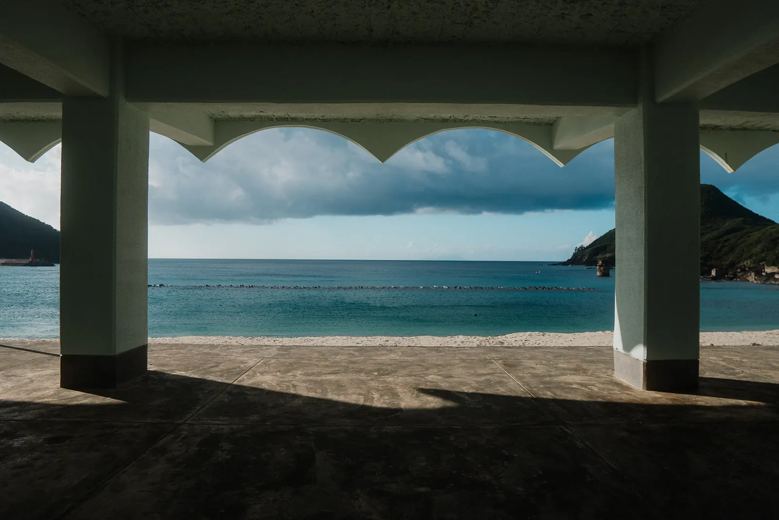 A concrete shelter framing the sea and a headland under heavy clouds.