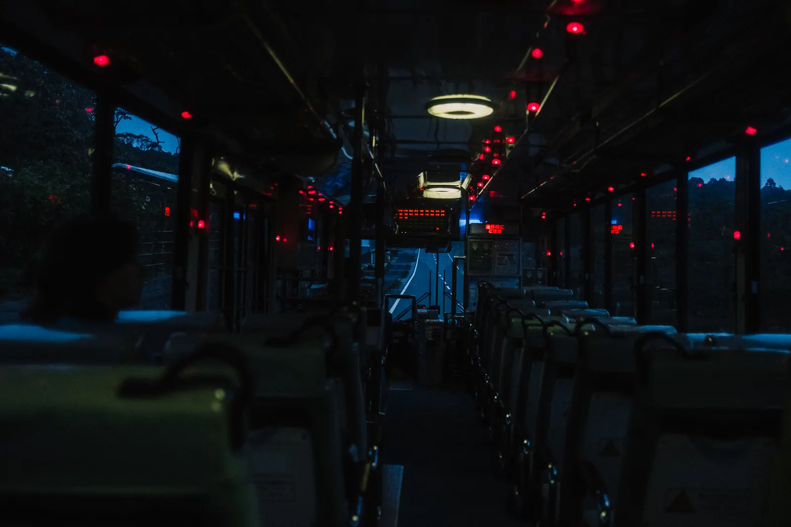 The aisle of a bus at dusk, red stop buttons glowing along the windows.