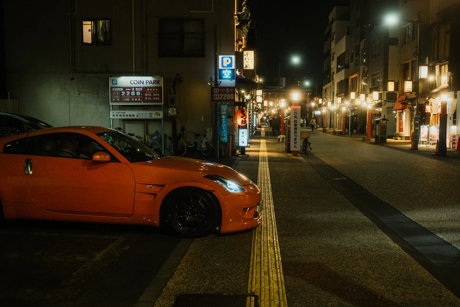 Orange Nissan 350Z nosing out into a lantern-lit street in Asakusa, Tokyo.