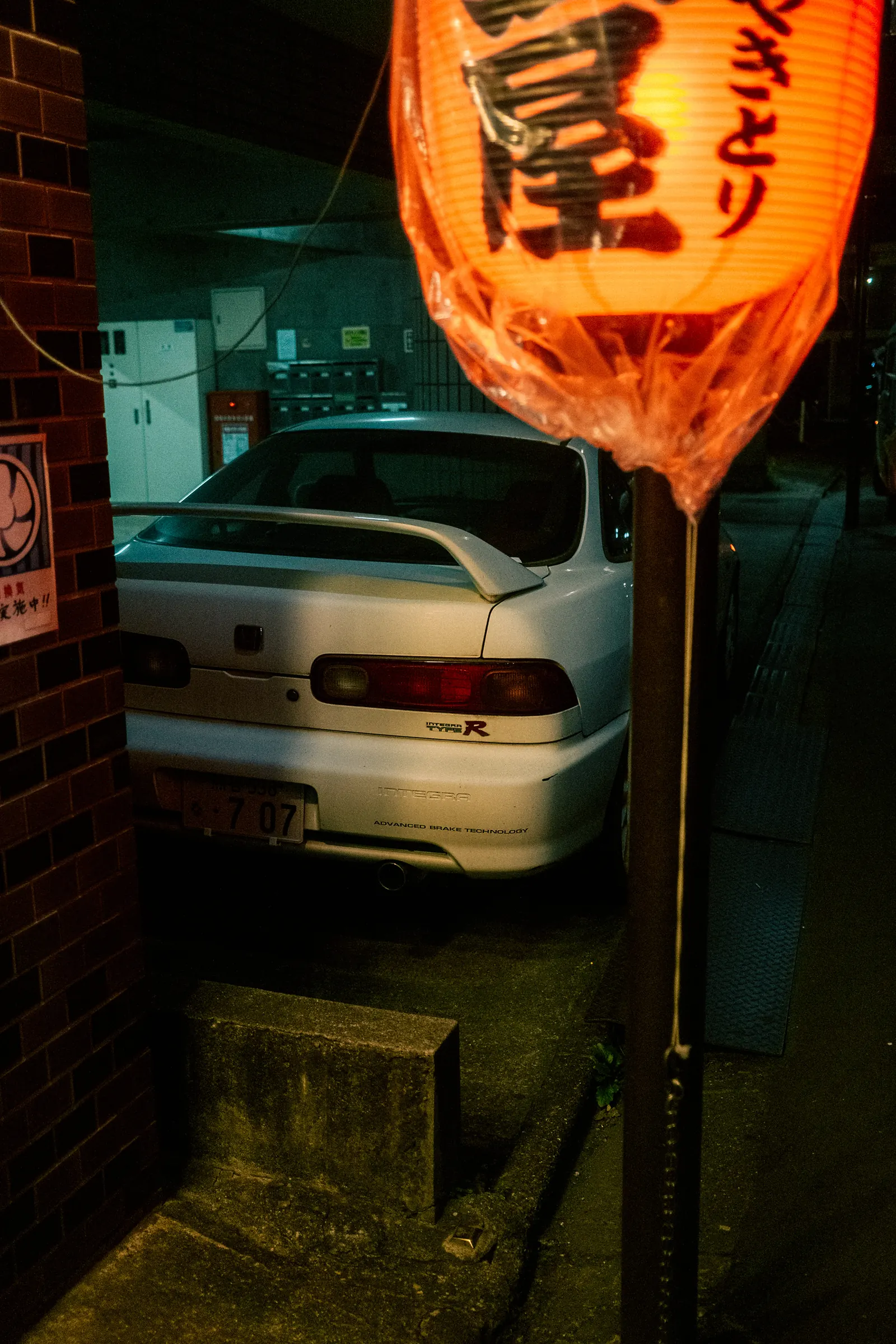 White Honda Integra Type R parked behind a glowing red paper lantern in a Tokyo side street.