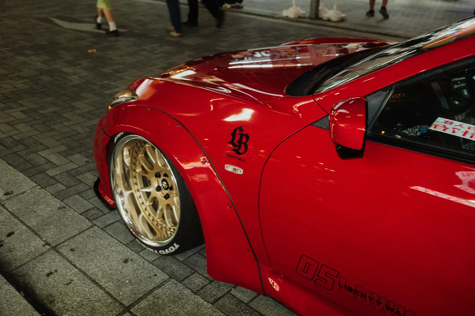 Red Infiniti Q50 with a Liberty Walk widebody kit and gold wheels on a Tokyo sidewalk.