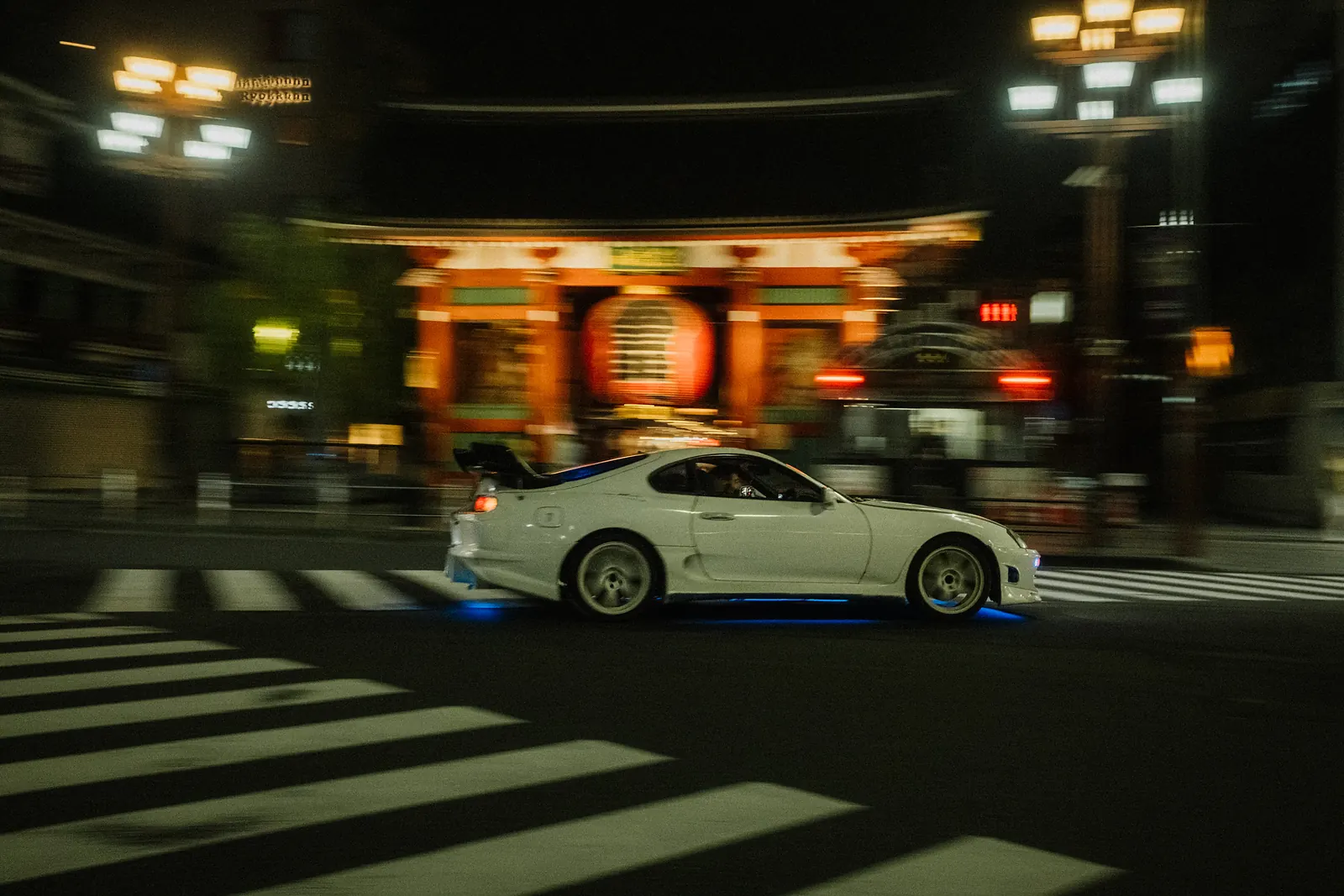 White Toyota Supra MK4 with blue underglow passing Kaminarimon gate in Asakusa, Tokyo.