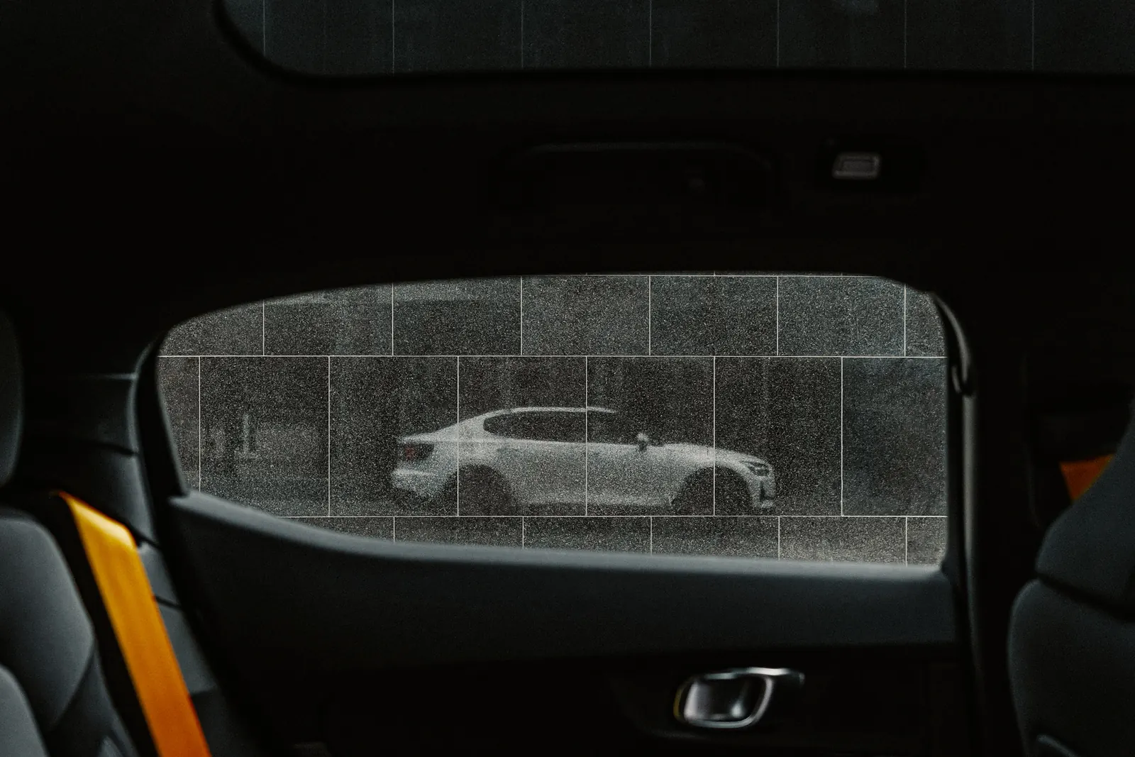 The Polestar 2's own silhouette reflected in a tiled shop window, seen through the car's rear window.