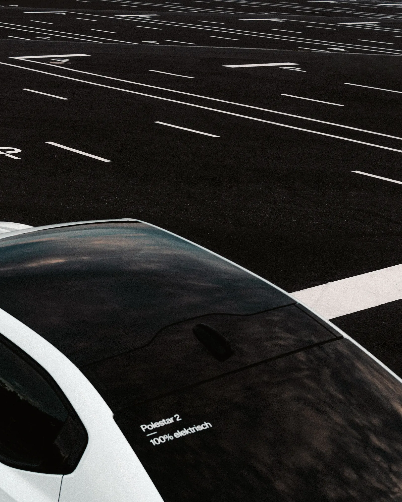A close-up of the Polestar 2's glass roof and badge, an empty striped parking lot beyond.