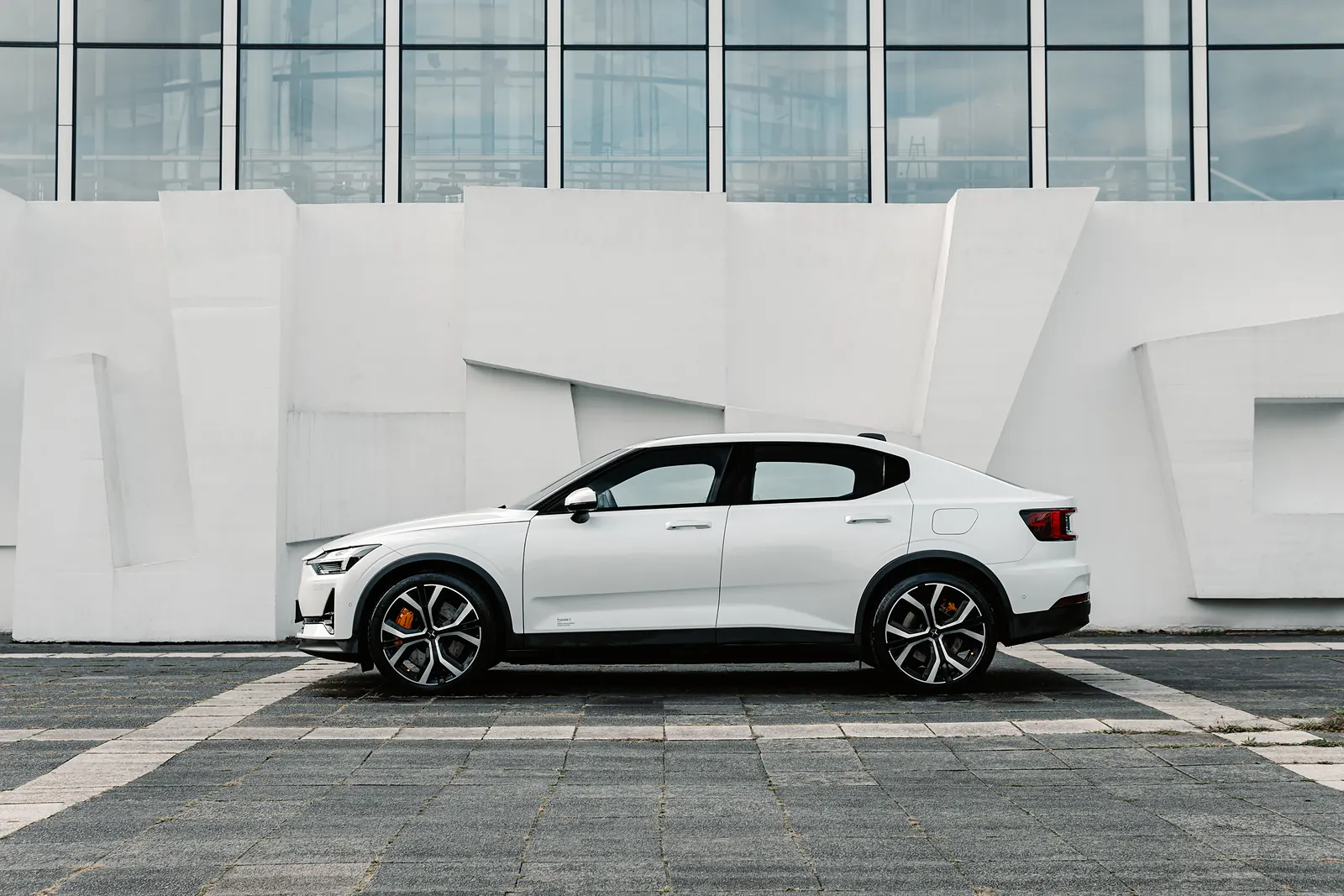 A white Polestar 2 in profile against an angular white concrete building.