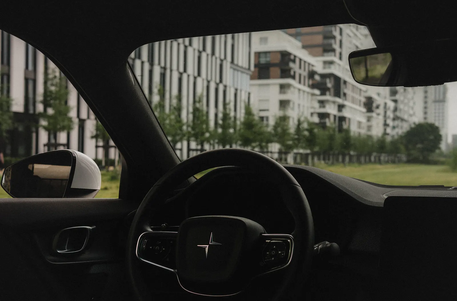 The view from the driver's seat over the Polestar-badged steering wheel toward apartment buildings outside.