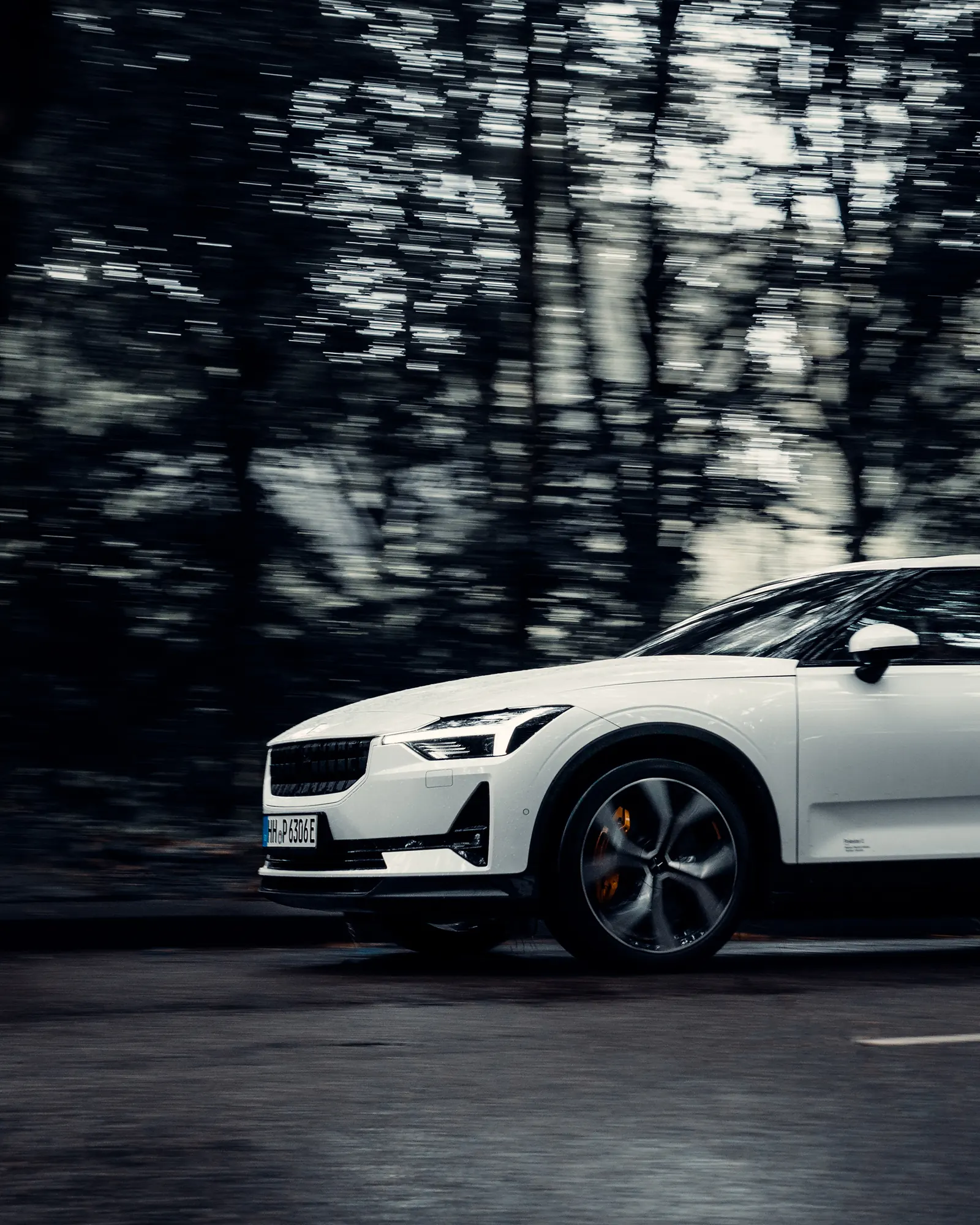 A white Polestar 2 driving fast along a forest road, trees blurred with motion.