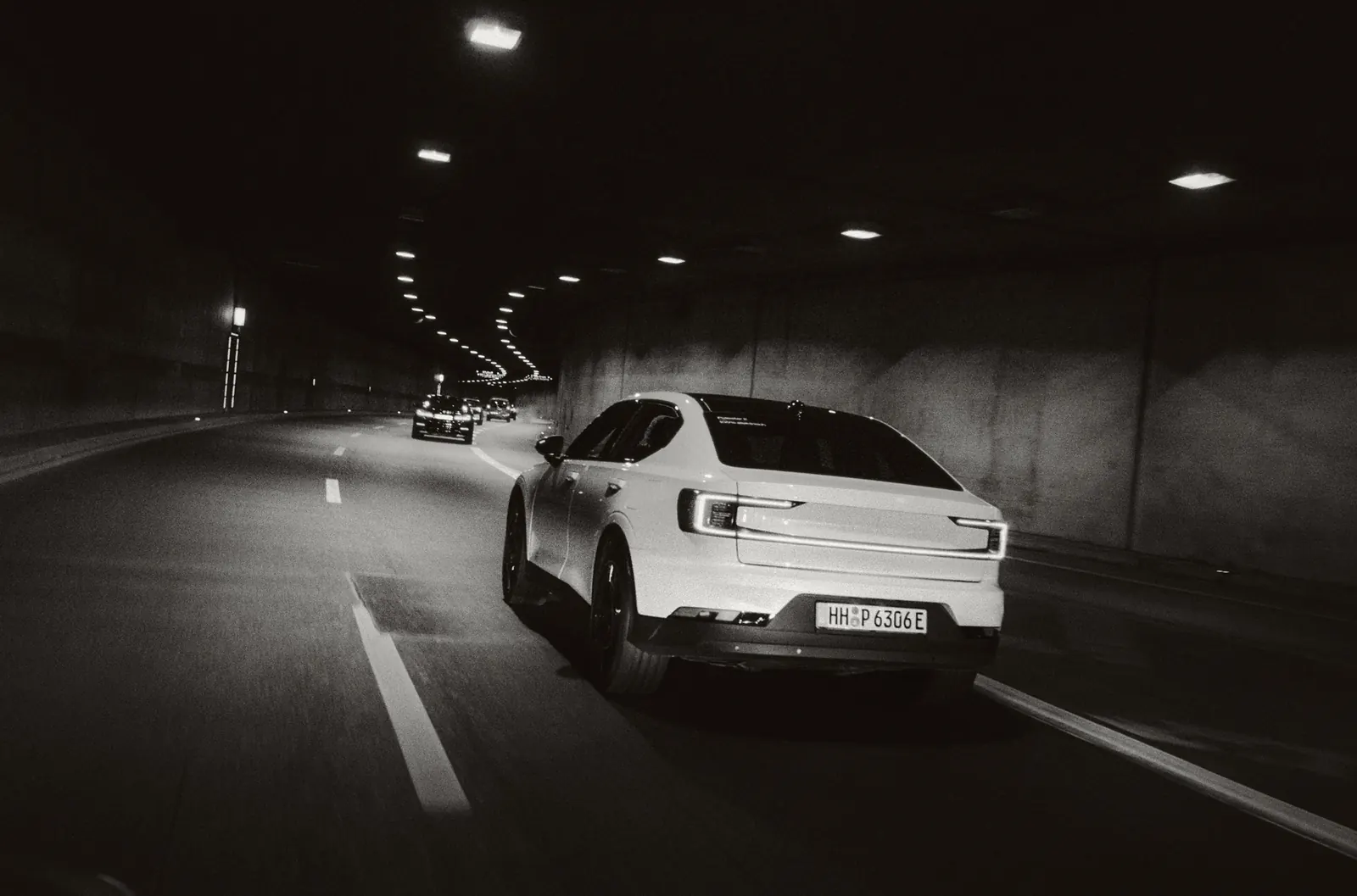 A white Polestar 2 driving through a tunnel at night, following cars glowing in the distance.