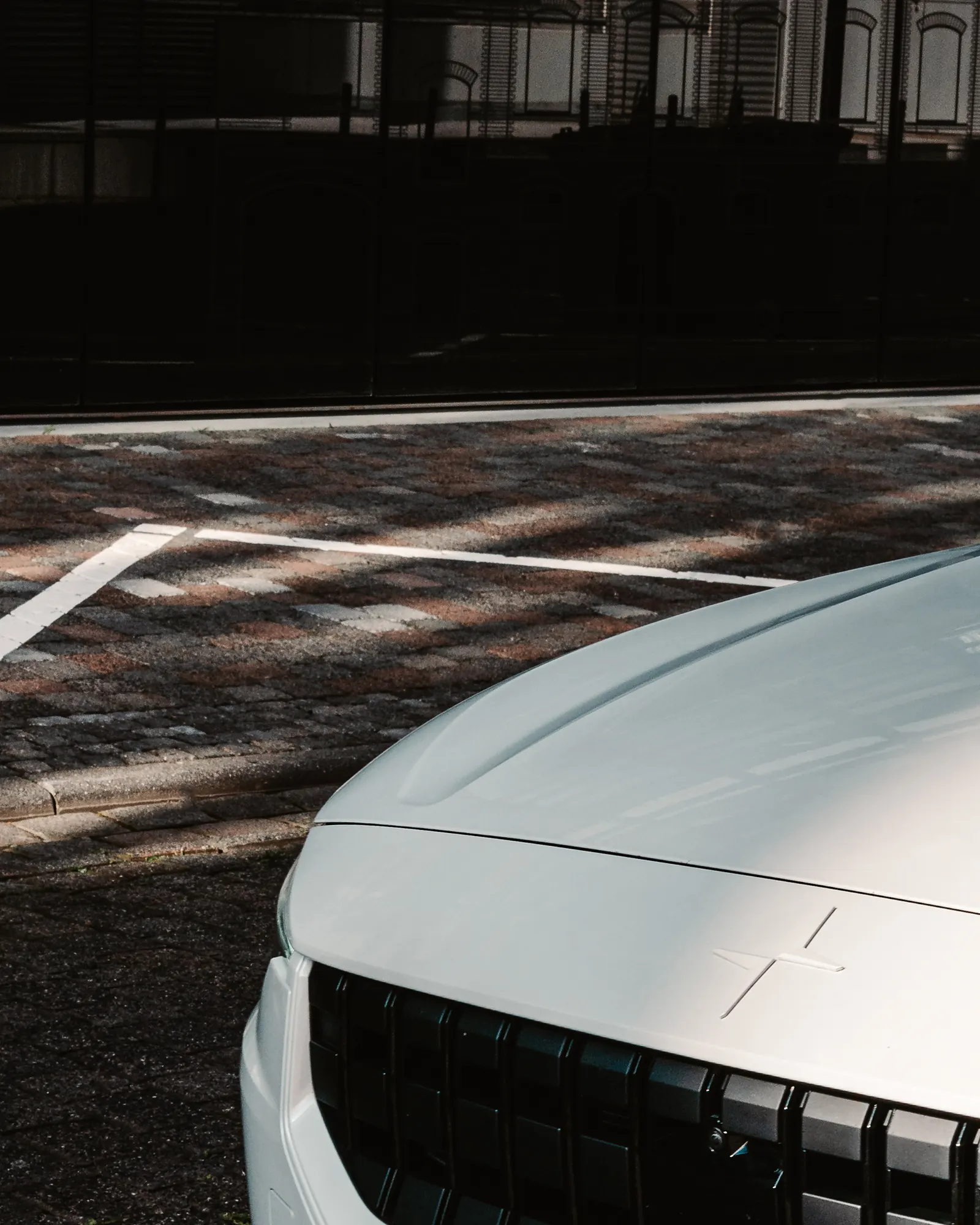 A close view of the Polestar 2's hood and grille from above, dappled shadows on the paving.
