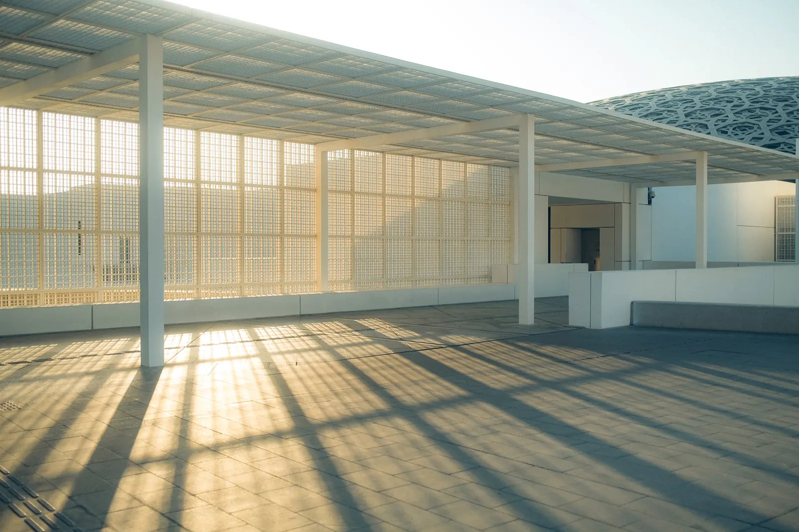 A colonnade of latticed screens at a museum, sunlight striping the stone floor.
