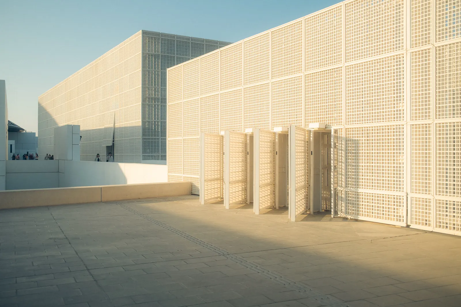 A lattice-clad museum building on Saadiyat Island, visitors walking along its rooftop terrace.