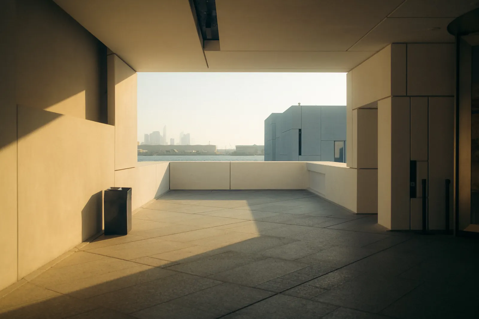 A shaded terrace opening onto the waterfront, the Abu Dhabi skyline visible across the water at dusk.