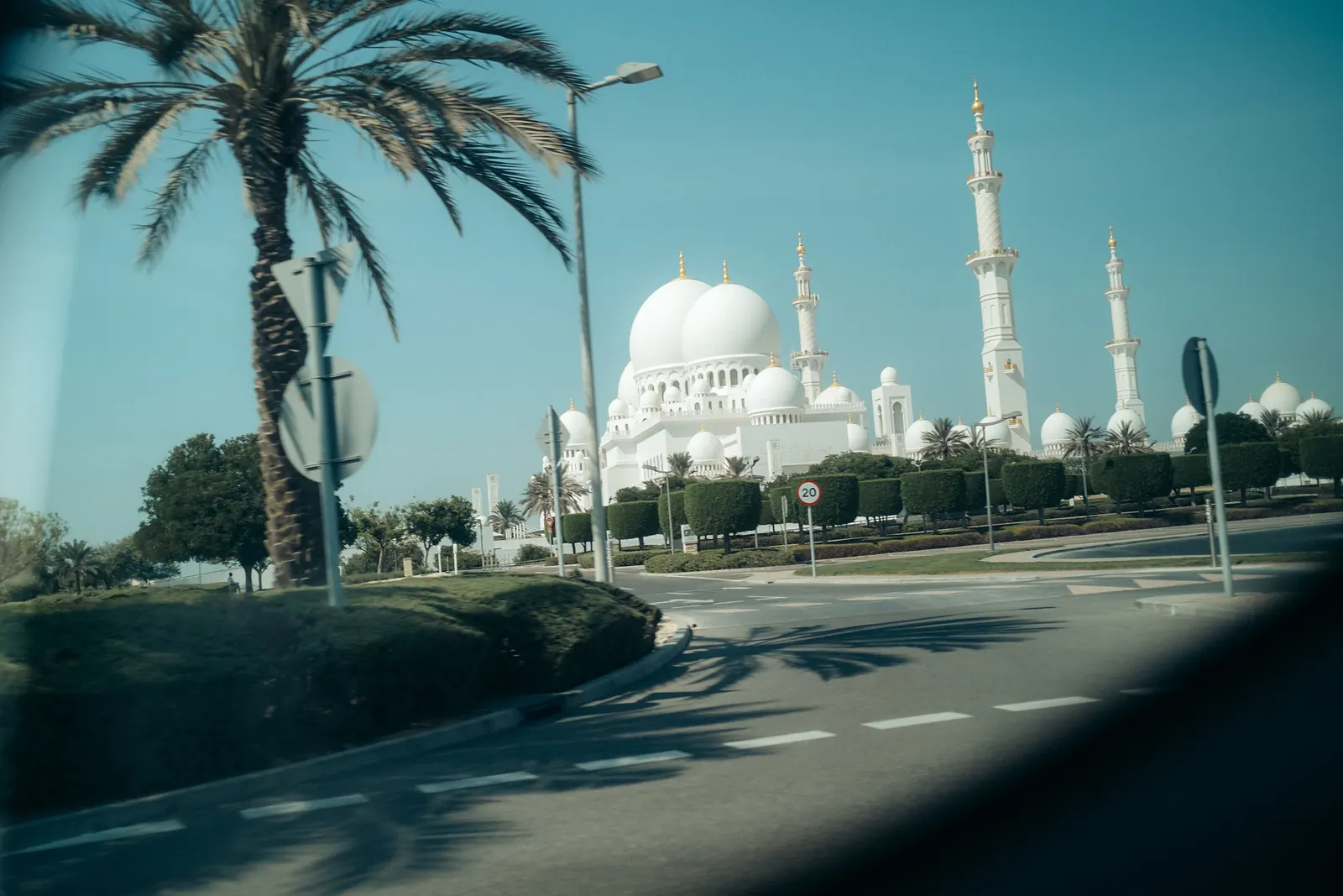 Sheikh Zayed Grand Mosque seen from a moving car, a palm tree framing the foreground.