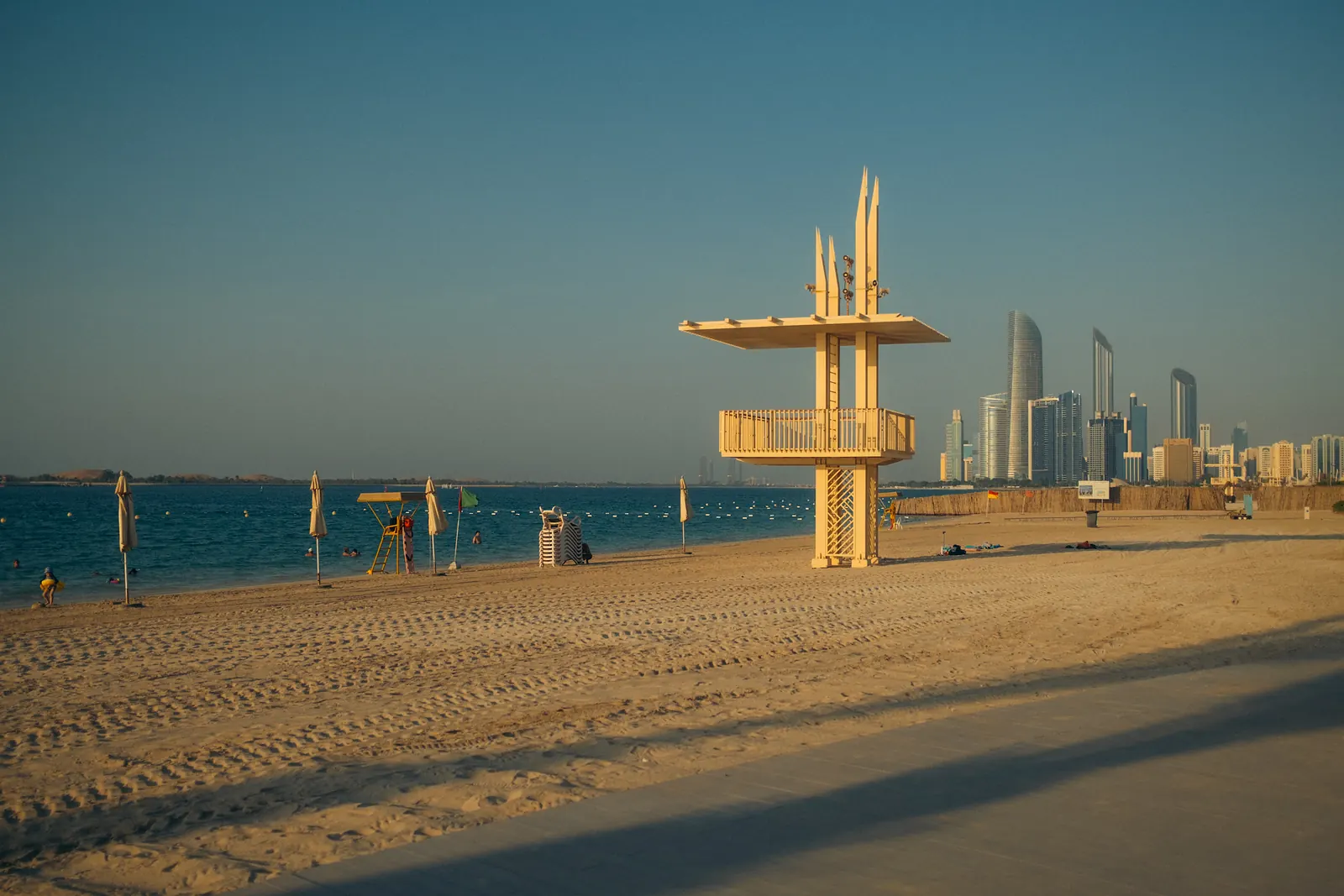 A lifeguard tower on an empty beach at sunset, the Abu Dhabi skyline across the water.